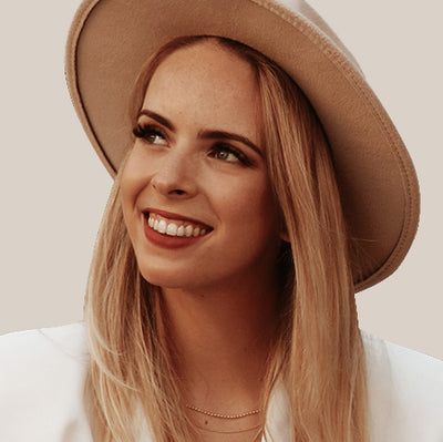 Woman wearing a beige hat and smiling against a plain background