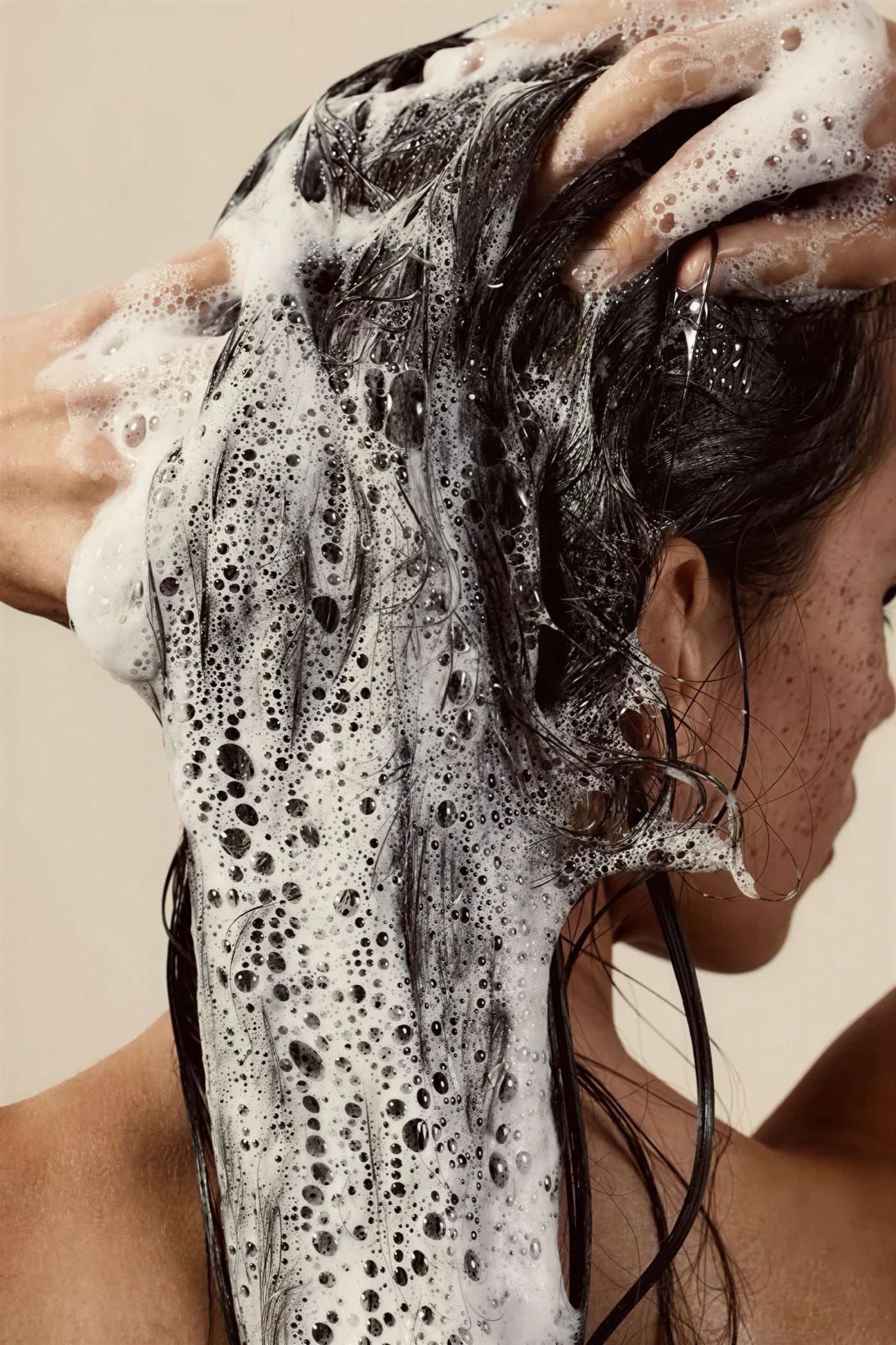 Person washing their hair with soapy water against a neutral background