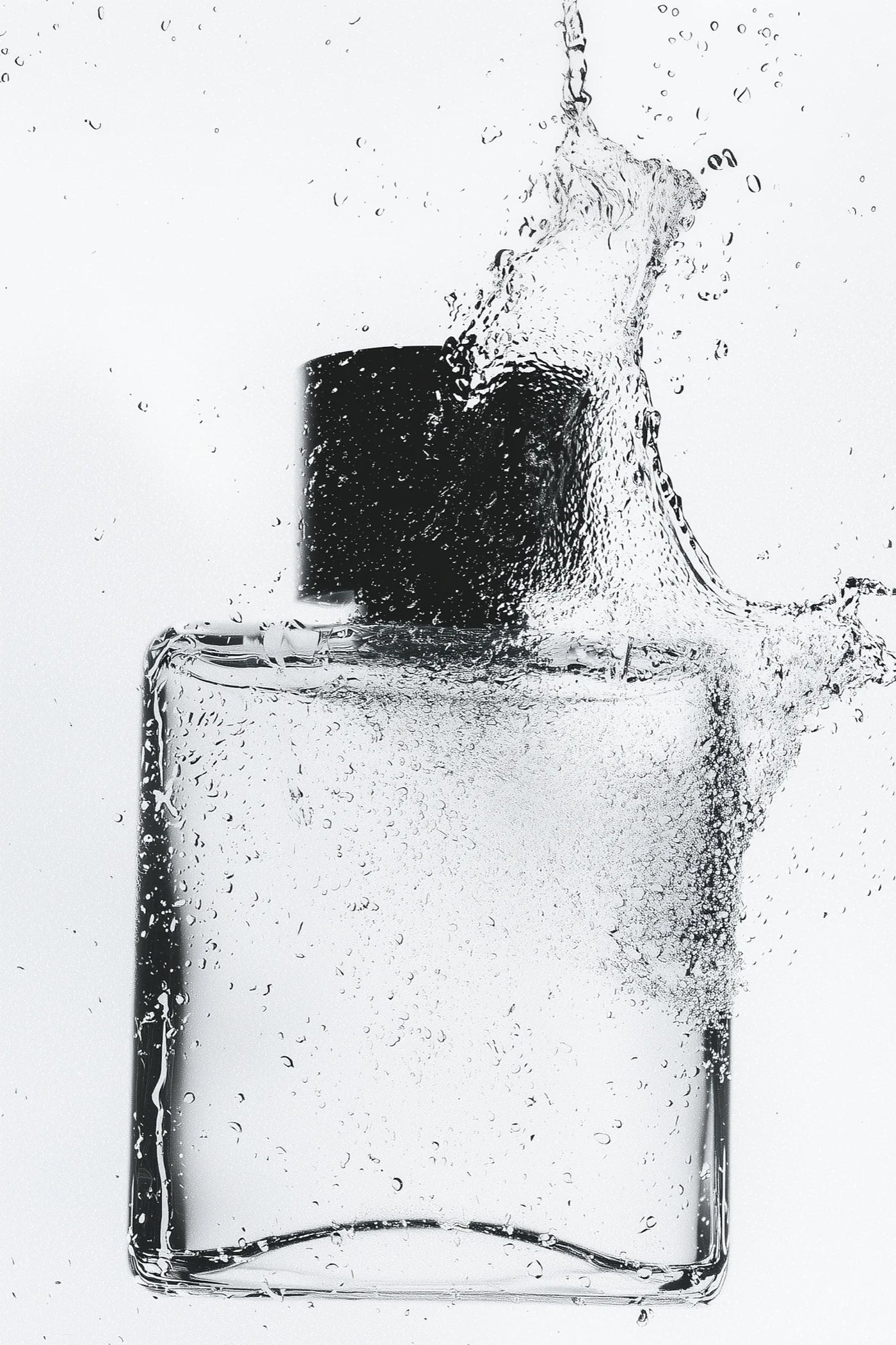 Clear glass bottle with black cap being splashed with water on a white background