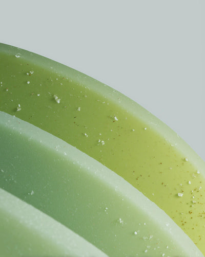 Close-up of a green soap bar with specks on a light gray background
