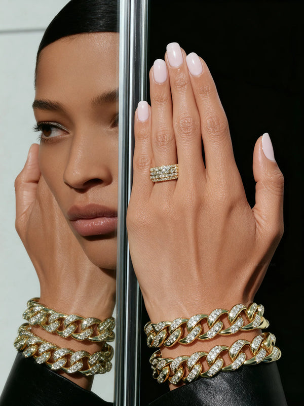 Woman's hand wearing gold chain bracelets and a ring, with a mirror reflection.