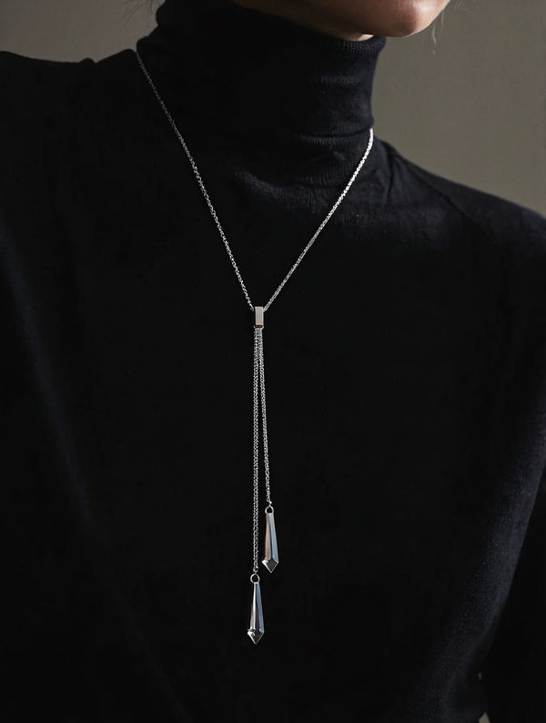 Person wearing a black turtleneck with a silver necklace featuring dangling pendants.
