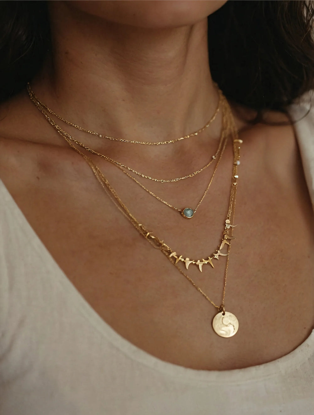 Close-up of a person wearing multiple gold necklaces with various pendants.