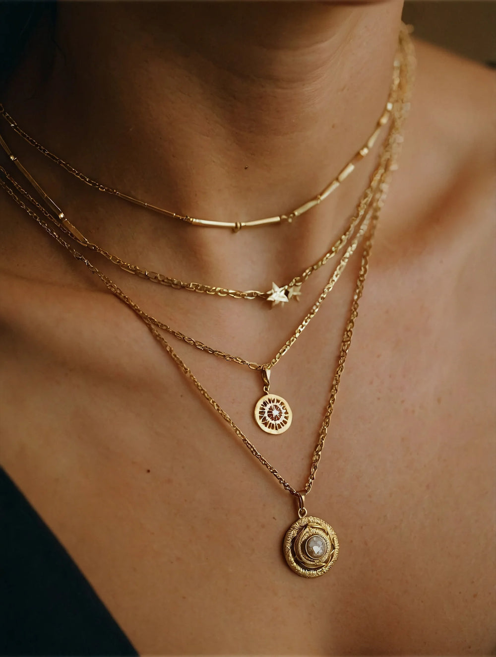 Close-up of a person wearing multiple gold necklaces with intricate designs.