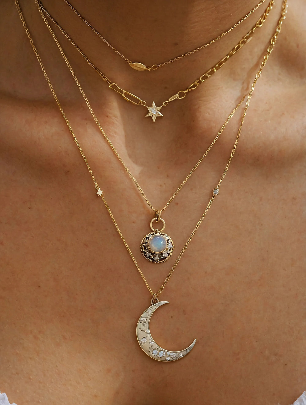 Close-up of a person wearing multiple gold necklaces with moon and star pendants.