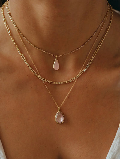 Two gold necklaces with teardrop pendants on a person's neck.