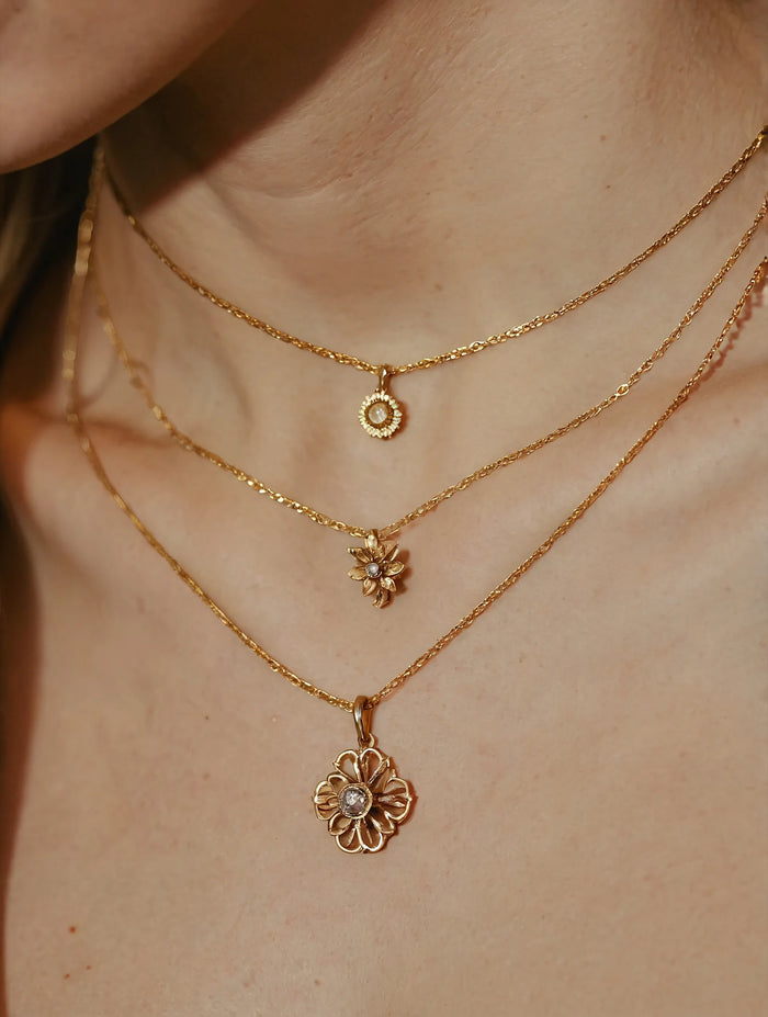 Close-up of a person wearing two gold necklaces with floral pendants on a neutral background