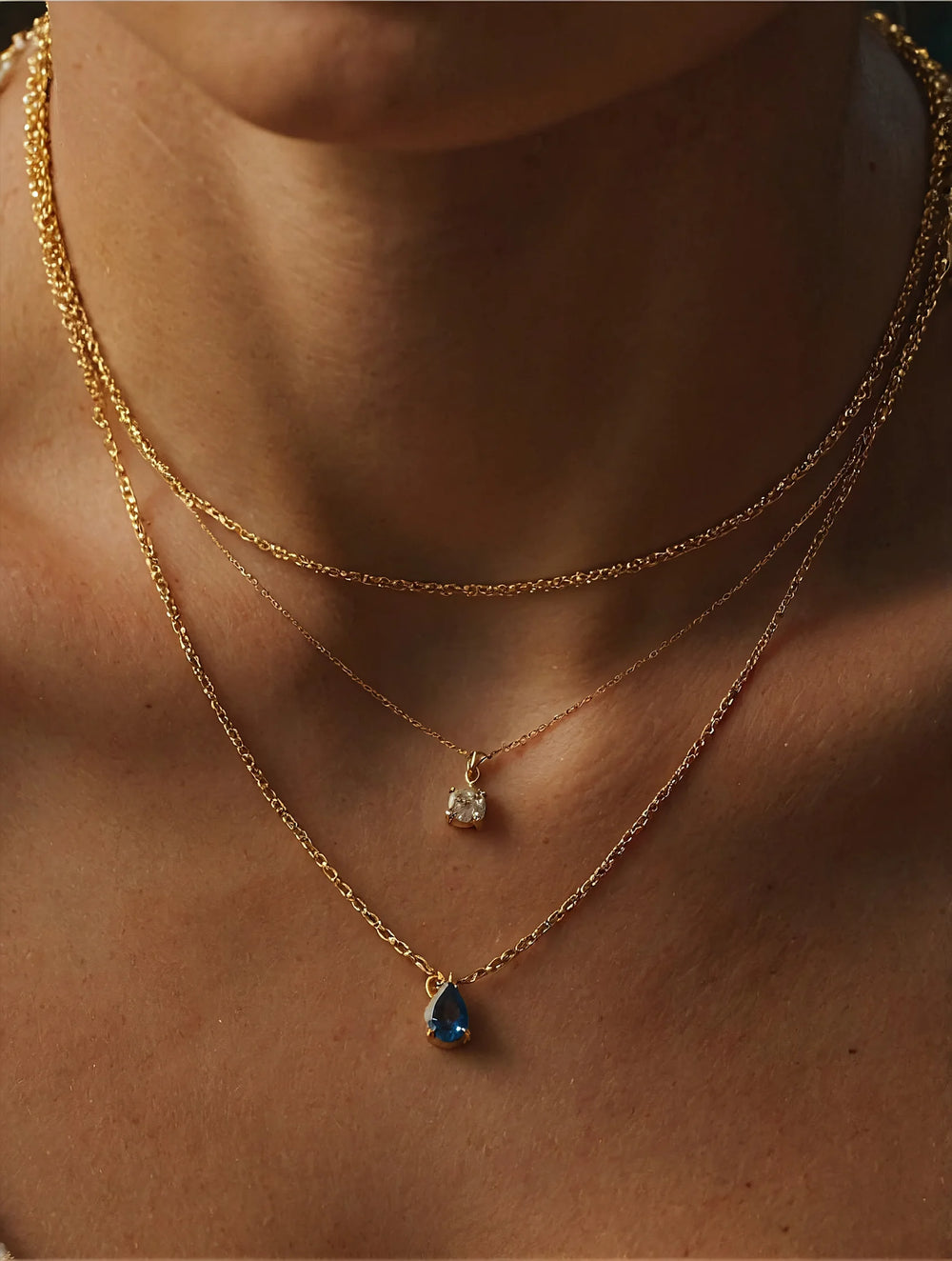 Close-up of a person wearing two gold necklaces with pendant stones on a neutral background