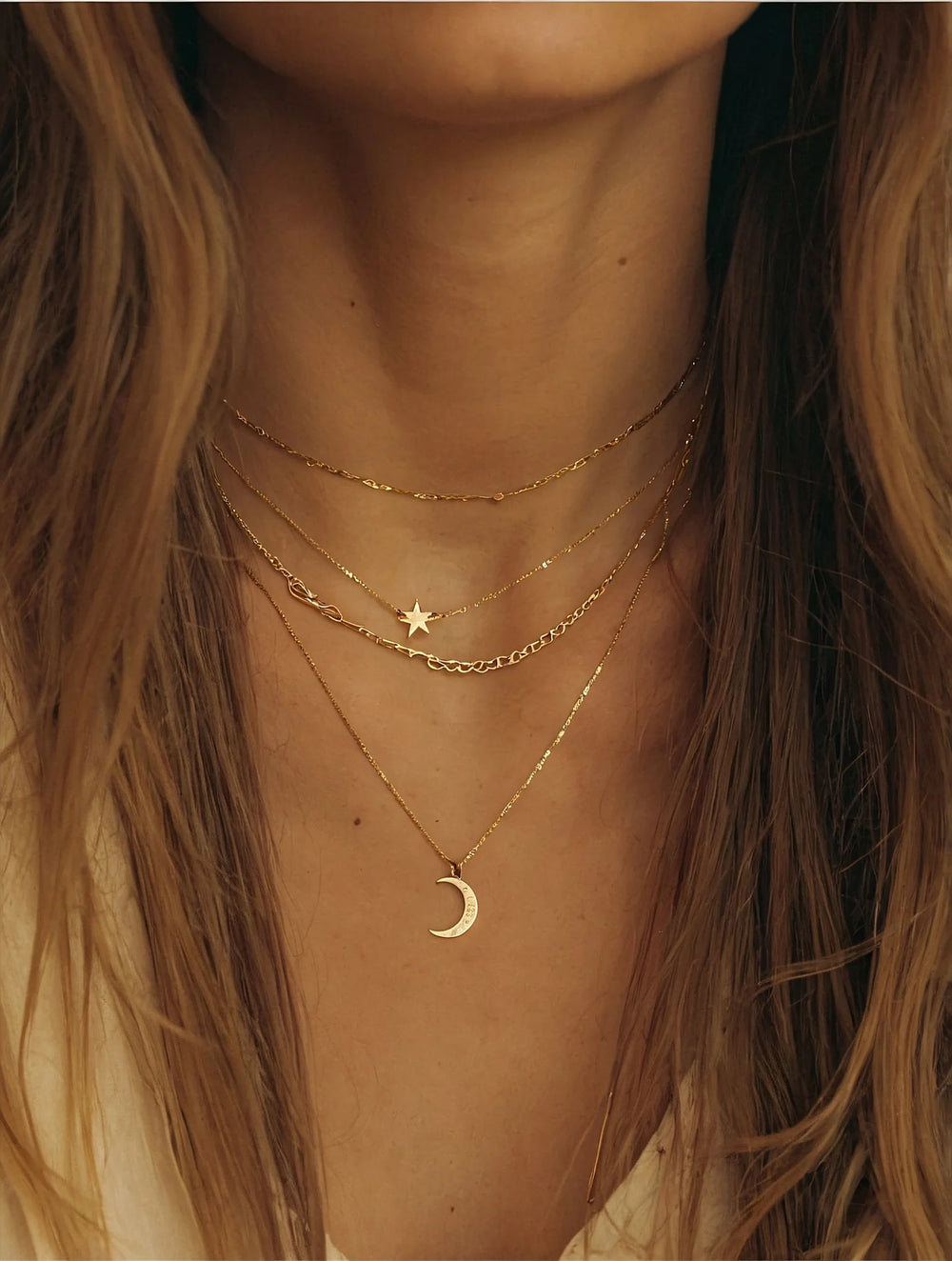 Close-up of a person wearing gold necklaces with star and moon pendants.
