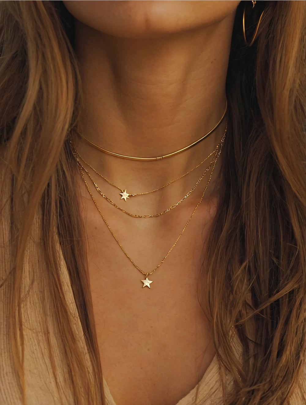 Close-up of a person wearing gold necklaces with star pendants.