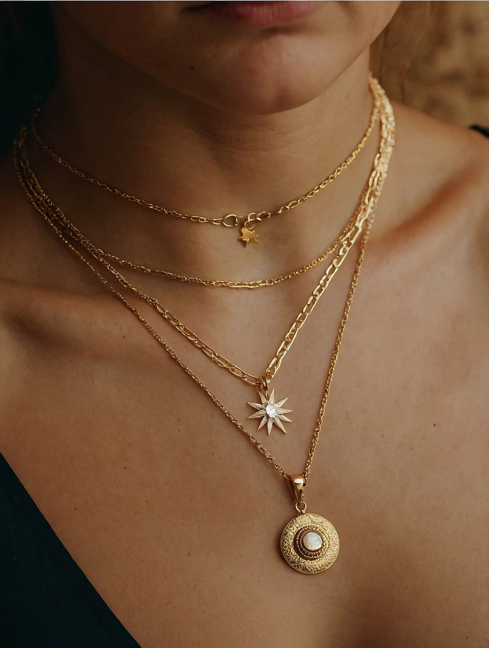 Close-up of a person wearing multiple gold necklaces with star and circular pendants.