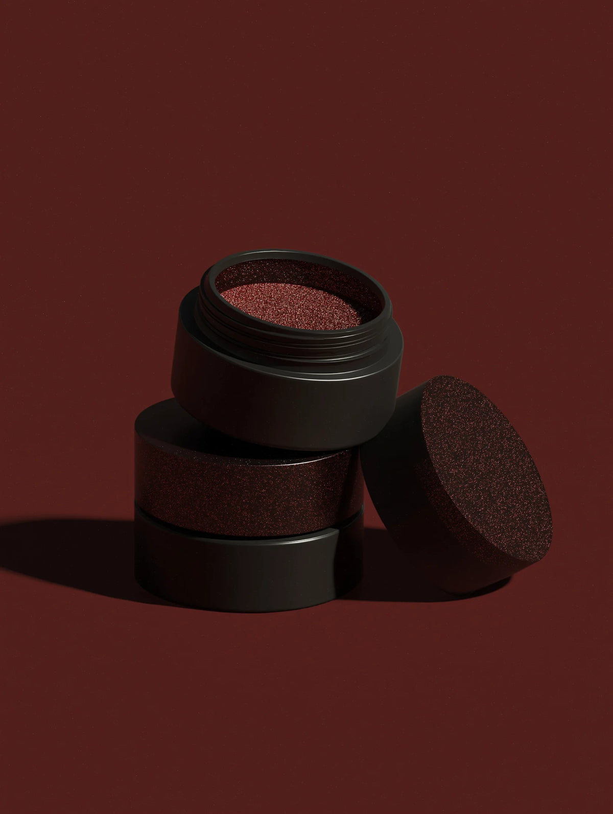 Three dark brown cosmetic containers stacked on a matching brown background