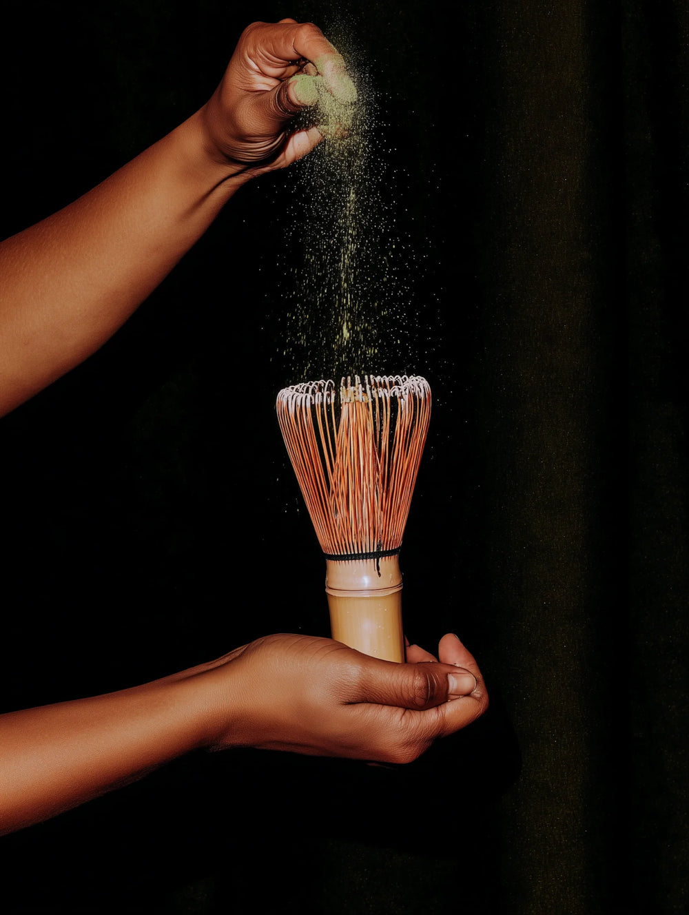 Person using a bamboo whisk to mix matcha against a black background