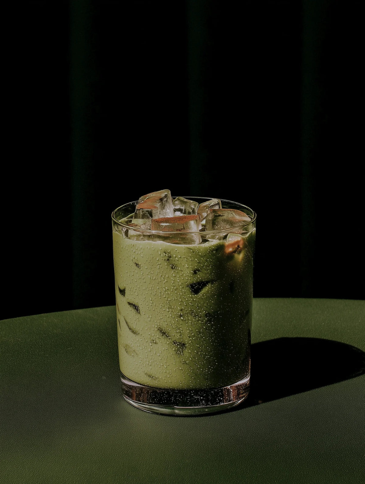 Glass of iced matcha with ice cubes on a dark background