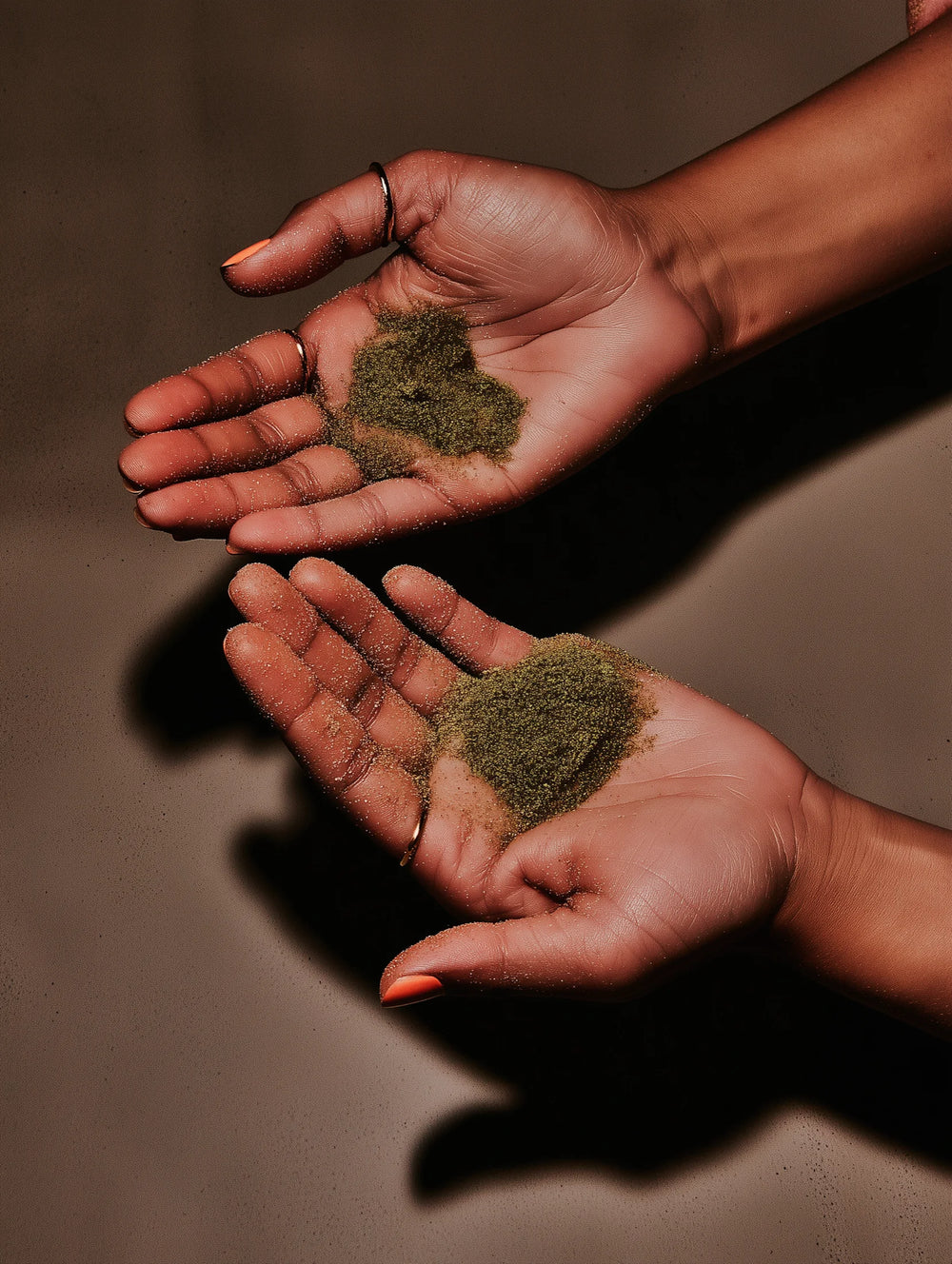 Two hands holding small amounts of matcha against a brown background
