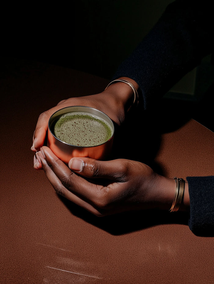 Hands holding a small metallic cup with matcha on a dark surface