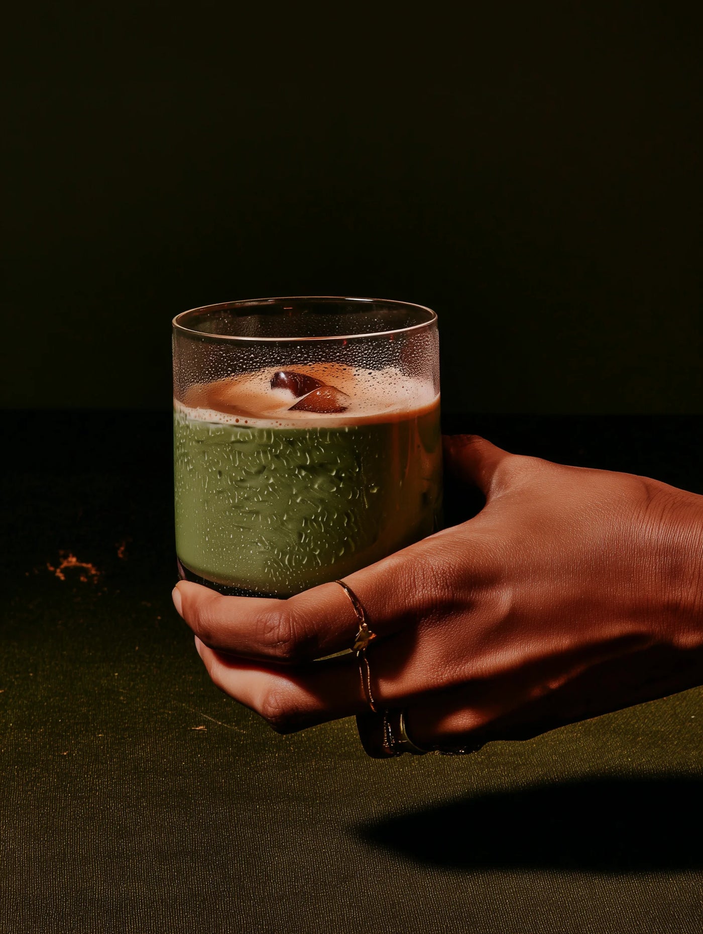 Hand holding a glass of matcha against a dark background