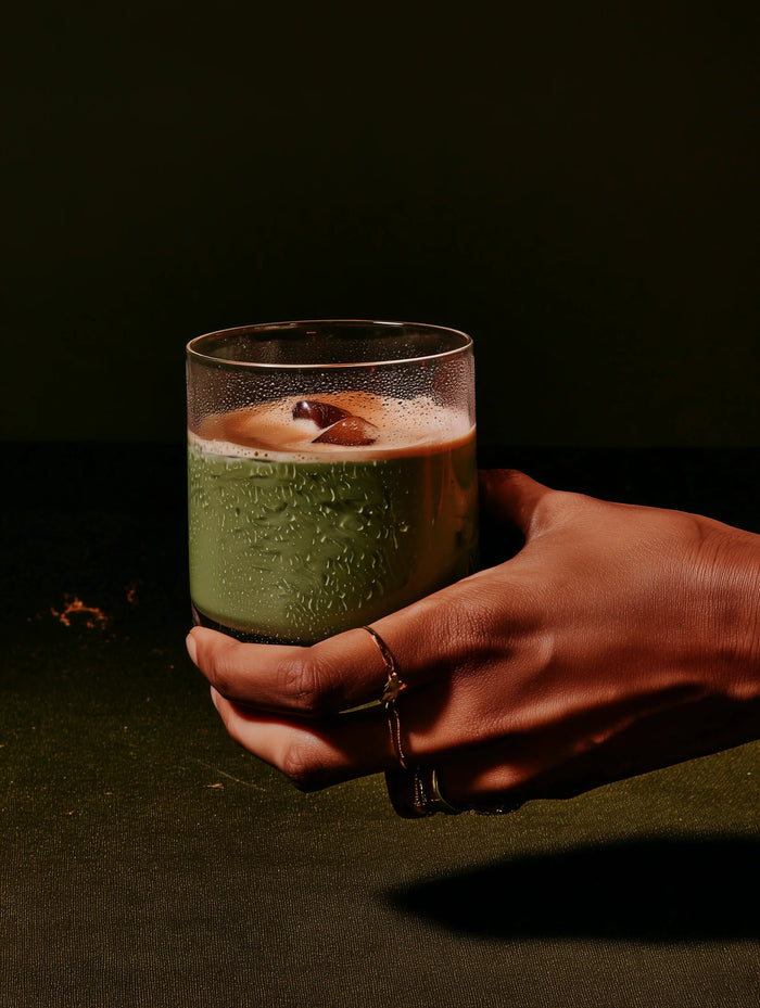 Hand holding a glass of matcha against a dark background