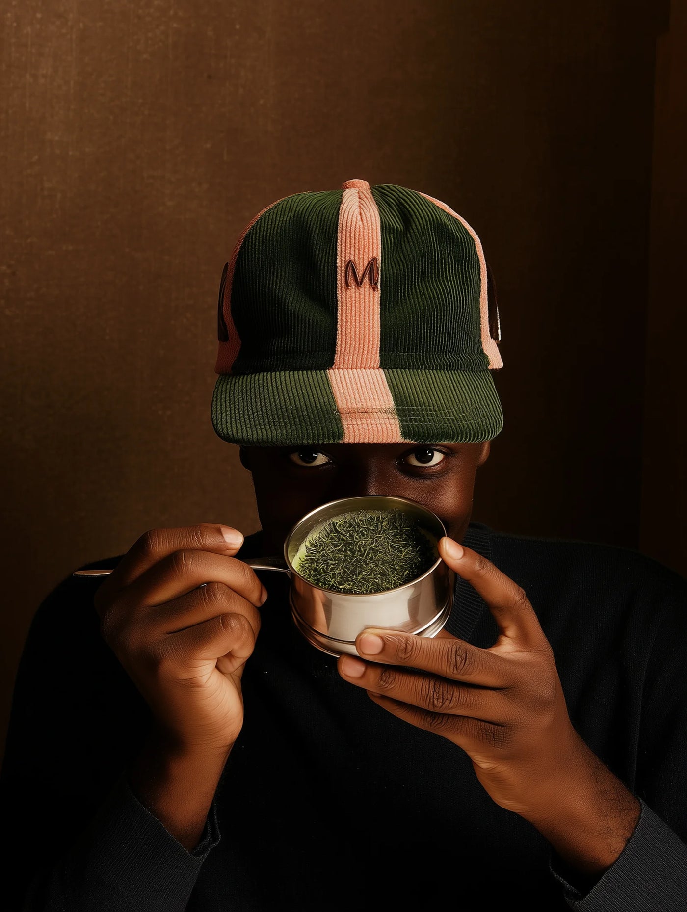 Person holding a metal cup with green powder against a dark background