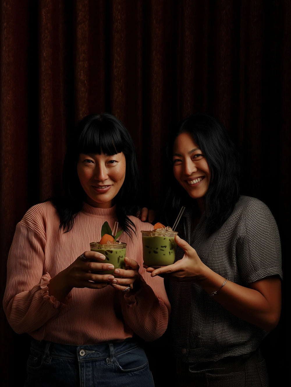 Two women holding matcha against a dark curtain
