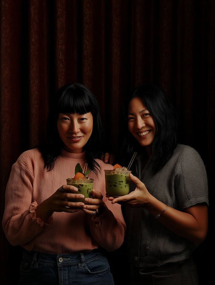 Two women holding matcha against a dark curtain