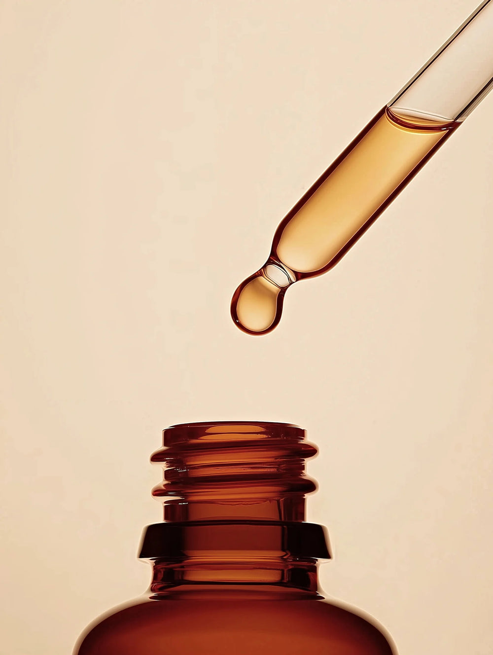 Amber glass dropper bottle with a droplet of liquid on a beige background