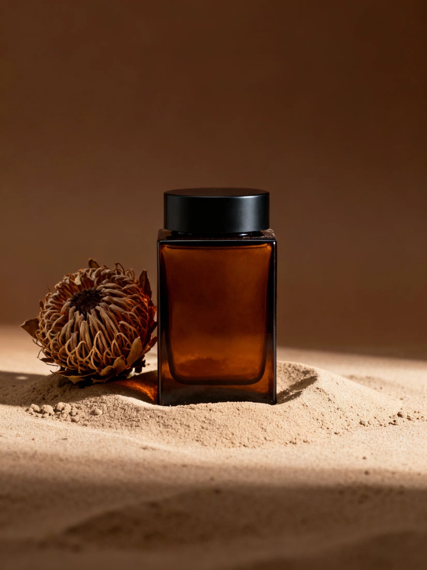 Amber glass jar with black lid on a sandy surface with a brown background