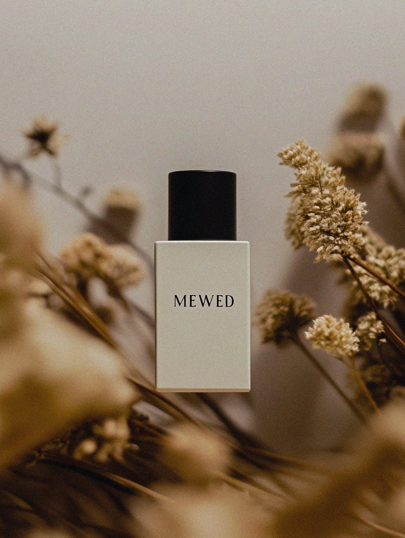 MEWED perfume bottle with dried flowers on a neutral background